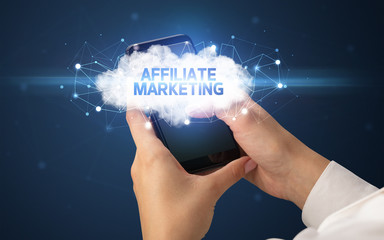 Female hand touching smartphone with AFFILIATE MARKETING inscription, cloud business concept