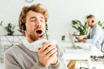 sick bearded broker with closed eyes sneezing near coworker in office