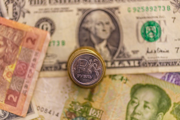 one ruble silver russian coin on a pile of coins and US and China notes. Small depth of field. China and the US fight for Russia