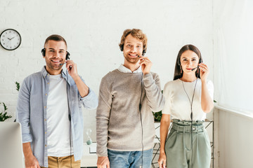 cheerful brokers in headsets standing and looking at camera