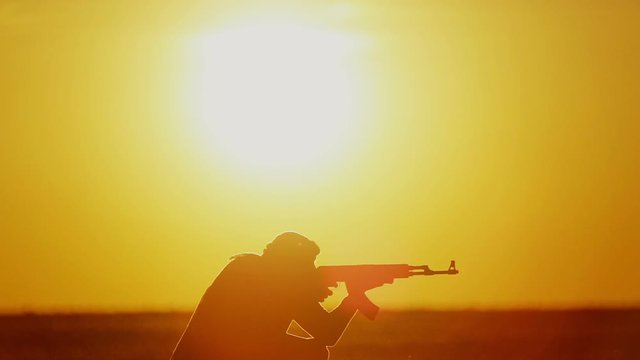 Islamic warrior with Kalashnikov at sunset day. Muslim fighter is training with a machine gun at sunset.
