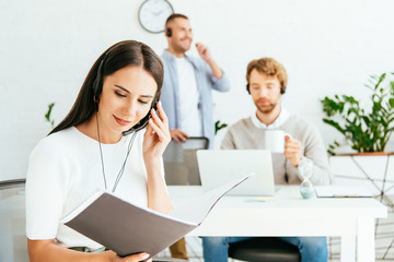 selective focus of happy broker looking at folder near coworkers in office