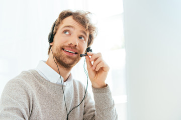 handsome bearded operator in brokers agency smiling and touching headset