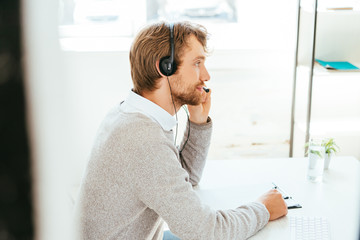 selective focus of handsome bearded operator in brokers agency touching headset