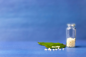 Homeopathic globules and glass bottle on a green plant leaf on blue background. The concept of healthcare and alternative herbal medicine: homeopathy and naturopathy. Flatlay, copyspace for text - obrazy, fototapety, plakaty