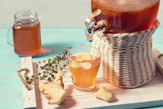 Fresh homemade kombucha fermented tea drink in a jar with faucet and in a cup and in mug on a white tray on a wooden background