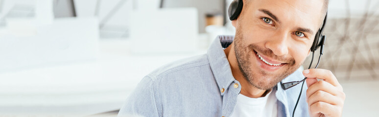 panoramic shot of happy operator in brokers agency touching headset and looking at camera