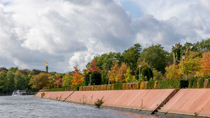 Fototapeta premium Autumn colors along the course of the Spree river with the Victory Column and a dramatic sky in the background, Berlin, Germany