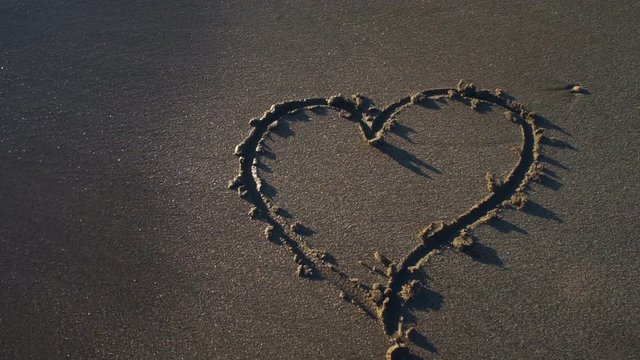 Heart symbol drawn by hand on sand washes away in wave