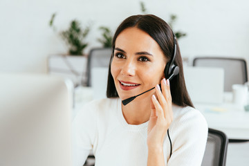 selective focus of attractive broker touching headset while working in call center