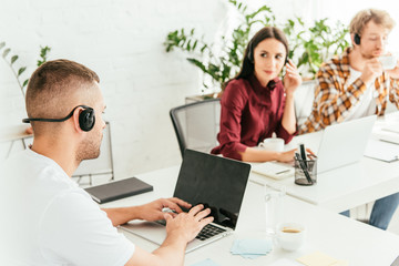 selective focus of broker typing on laptop keyboard near coworkers in office