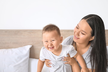 Asian mother and cute little baby playing on bed