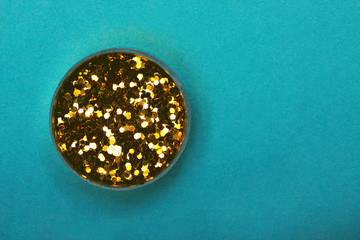 Jar with golden sparkles on a turquoise trendy background. Stylish place for text about glamour, beauty industry, holiday.