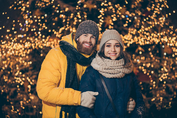 Photo of two sweethearts pair guy lady in love visit city lighted park newyear x-mas night frosty weather stand close wear warm winter jackets scarfs hats outdoors