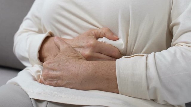 Mature female holding hands on tummy, abdominal pain, gastritis health problem