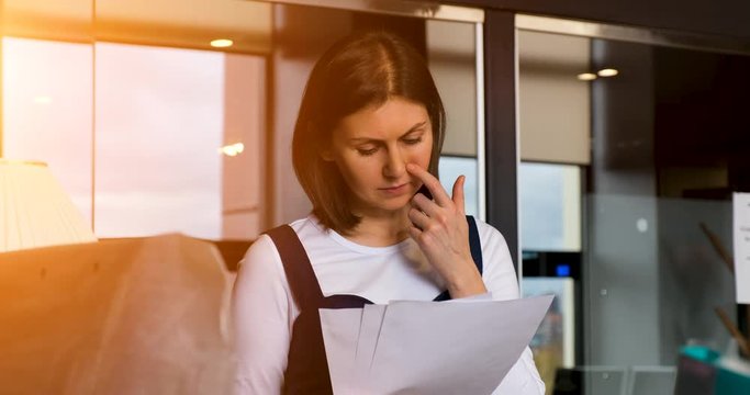 the young woman works in the office with papers and a notebook. outside the window is the evening sun. image in warm sunny color. slow motion 4k 25p prores 422