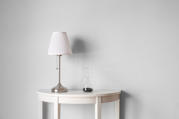 Table with lamp and hourglass near white wall