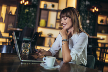 Busy woman using credit card for shopping and paying bills on line while sitting in coffee shop