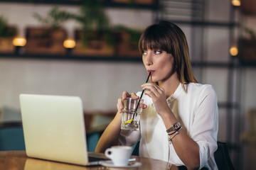 Portrait of a young beautiful businesswoman enjoying coffee during work on portable laptop computer