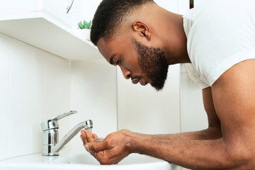 Black guy washing face in bathroom, side view