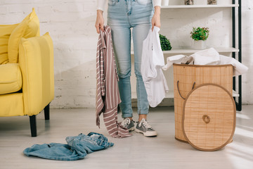 Fototapeta na wymiar cropped view of housewife in denim jeans holding clothes while standing near laundry basket