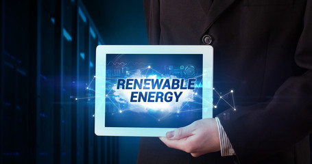 Young business person working on tablet and shows the inscription: RENEWABLE ENERGY