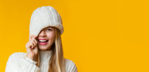 Portrait of girl in winter hat flirting over yellow background