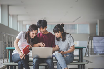 Education concept - University students sit at a desk with books and laptops. Asian young people are attentively studying on the internet. Happy young people doing group study in school.