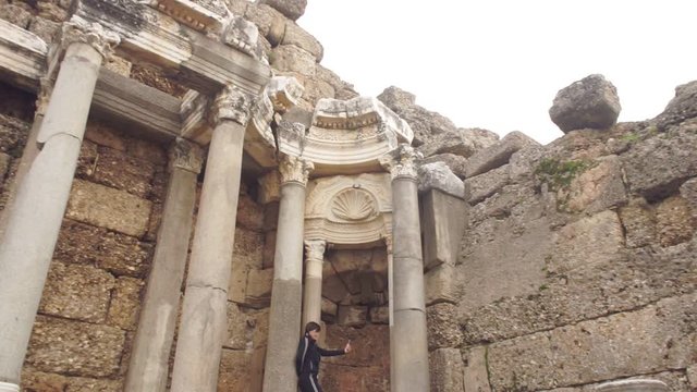 girl in tracksuit makes selfie at stone columns by old wall