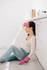 tired housewife sitting on floor in kitchen with closed eyes