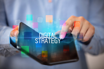 Young man holding a foldable smartphone with DIGITAL STRATEGY inscription, educational concept