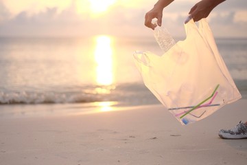 Hands collecting plastic in a white plastic bag on the beach. Polluting the ocean .People who help...