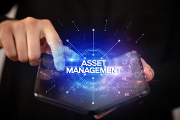 Businessman holding a foldable smartphone with ASSET MANAGEMENT inscription, new business concept