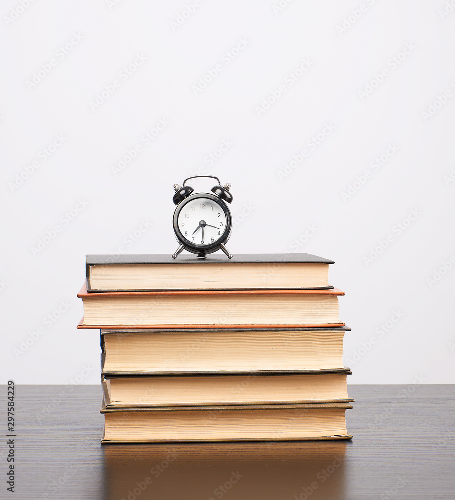 Poster stack of books and a black alarm clock on the table