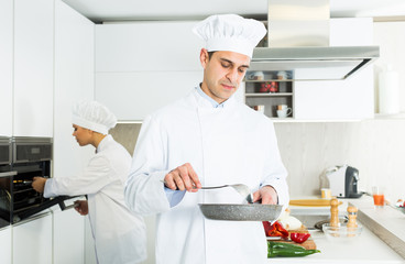 Male cook with stewpot working on kitchen with woman cook