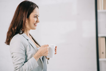 smiling, young secretary looking away while holding coffee cup