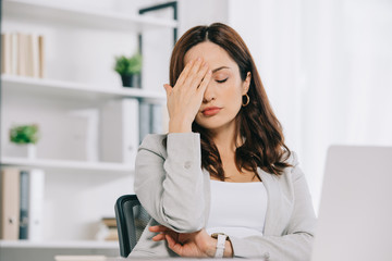 Obraz premium exhausted secretary suffering from headache while sitting with closed eyes and holding hand near head