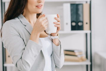 cropped view of young secretary holding coffee cup in office