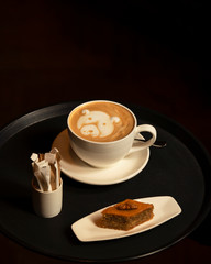 cup of cappuccino with dog latte art served with pakhlava in dark background