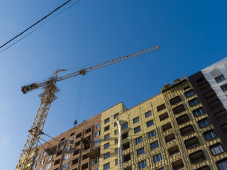 Bottom view of the construction of the house. Tower crane. The theme of an emerging housing market under construction