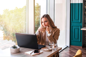 Beautiful business woman sitting in cafe and working. There are laptop, smartphone and cup of coffee. Woman enjoying her coffee while working.