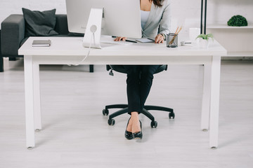 patial view of secretary in high heeled shoes sitting at workplace in office chair