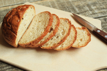 Sliced ​​cereal bread lies on a wooden board. Nearby lies a knife.