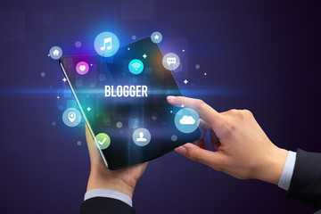 Businessman holding a foldable smartphone with BLOGGER inscription, social media concept