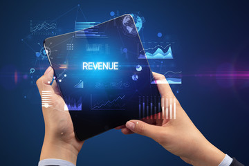 Businessman holding a foldable smartphone with REVENUE inscription, successful business concept
