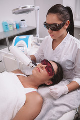 Vertical shot of a professional beautician and female client wearing protective glasses during...
