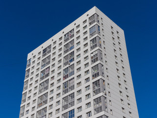 View of a new white residential building on a background of blue sky. The theme of an emerging housing market under construction