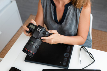 Naklejka premium Business and creativity. A woman looks at the pictures on the camera. Nearby lies a tablet and glasses. Top view