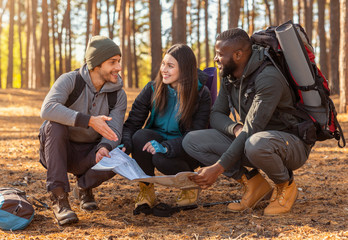 Friends with backpacks sitting around map in forest