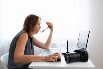 Business and creativity. Young woman working on a laptop. On the table is a camera and a tablet